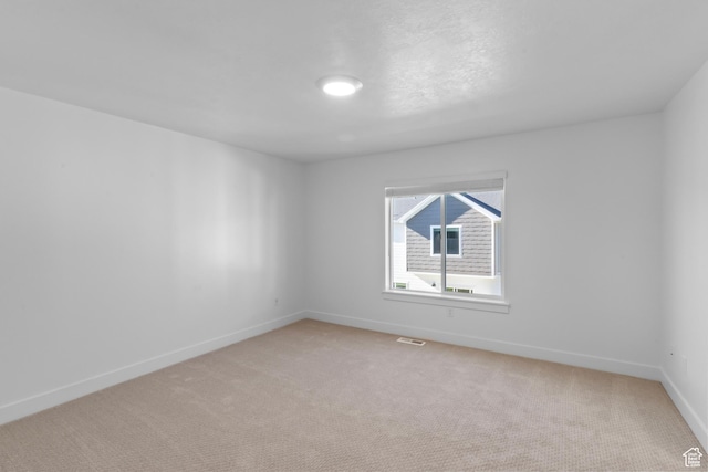 spare room featuring visible vents, light carpet, and baseboards