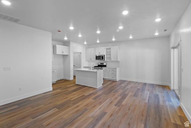 kitchen featuring white cabinets, appliances with stainless steel finishes, visible vents, wood finished floors, and a center island with sink