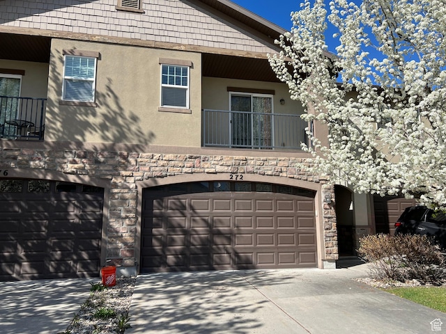 view of front of house with stucco siding, a balcony, concrete driveway, and stone siding