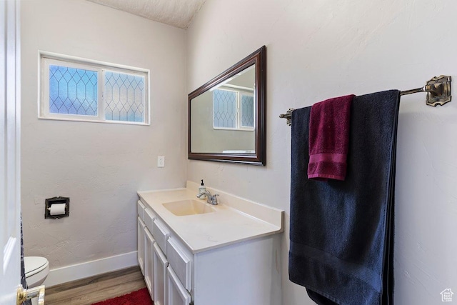 half bathroom featuring baseboards, wood finished floors, toilet, and vanity