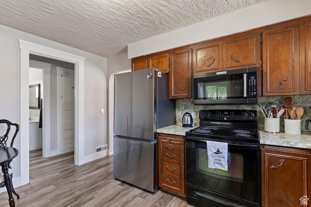kitchen featuring freestanding refrigerator, light countertops, backsplash, visible vents, and black electric range oven
