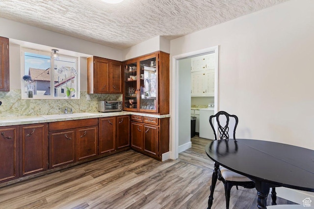 kitchen featuring wood finished floors, light countertops, backsplash, a sink, and washer / clothes dryer