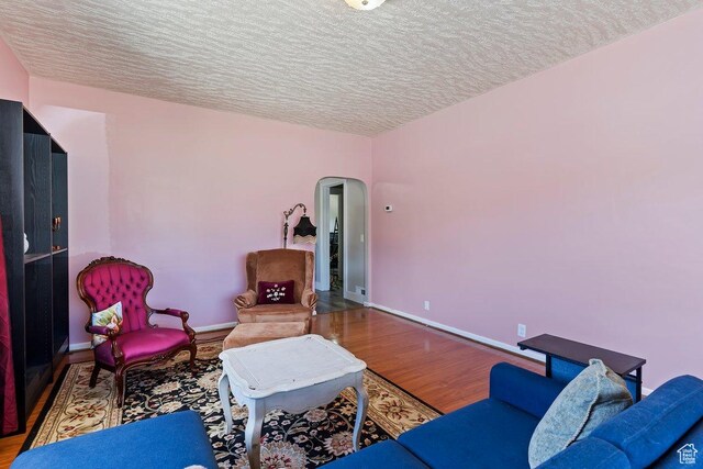 sitting room featuring baseboards, wood finished floors, a textured ceiling, and arched walkways