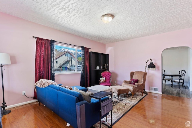 living room with a textured ceiling, visible vents, baseboards, arched walkways, and wood finished floors