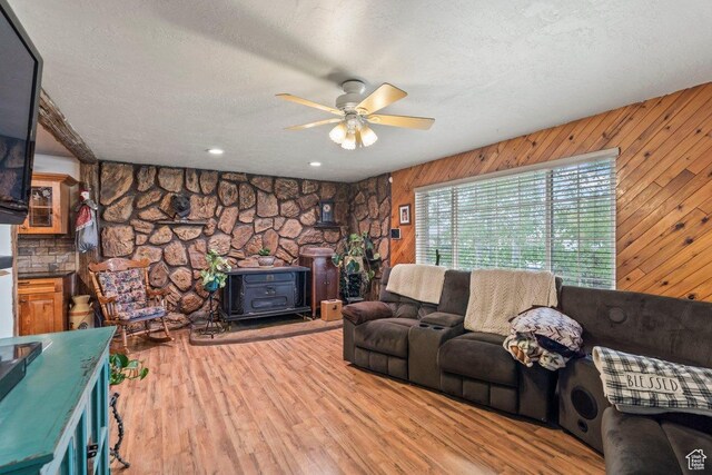 3168 W 1300 N, Clinton, UT 84015 - living area with a wood stove, wooden walls, a ceiling fan, a textured ceiling, and wood finished floors