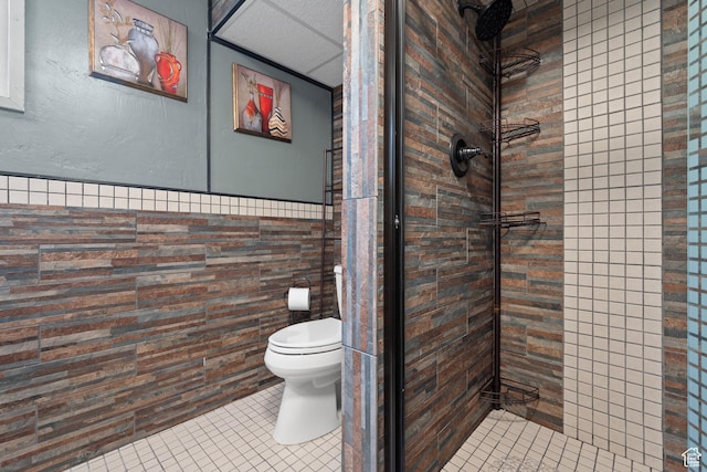 bathroom featuring tile patterned floors, toilet, a wainscoted wall, and a stall shower