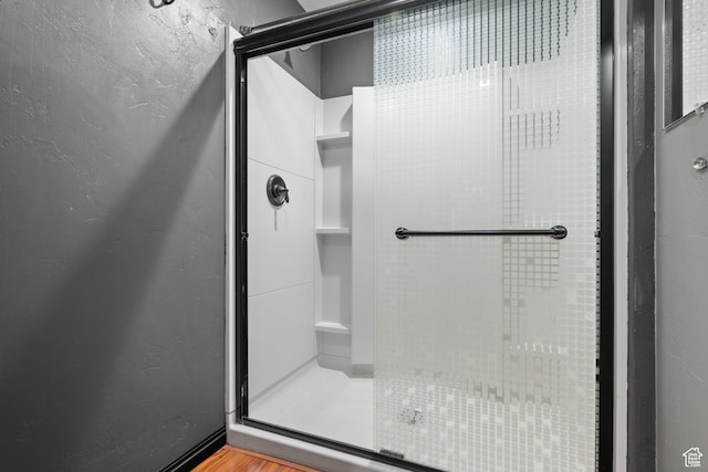 bathroom with a textured wall, a shower stall, and wood finished floors