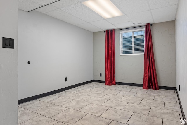 unfurnished room with a paneled ceiling and baseboards
