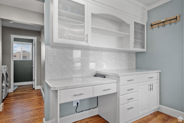 unfurnished office with crown molding, washing machine and clothes dryer, wood finished floors, and baseboards