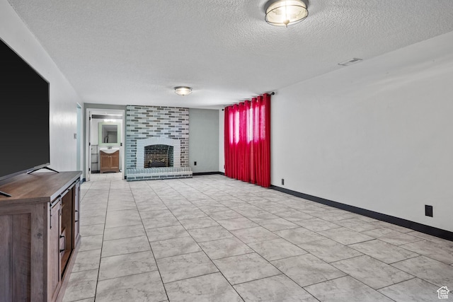 unfurnished living room with a fireplace, a textured ceiling, visible vents, and baseboards