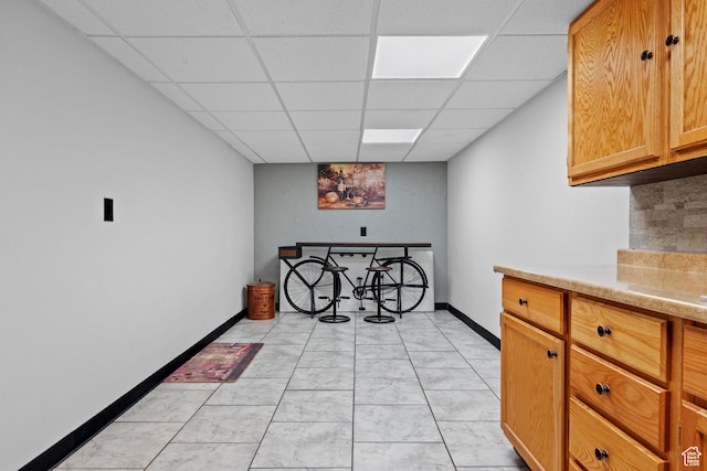 interior space with baseboards, decorative backsplash, light countertops, and a paneled ceiling