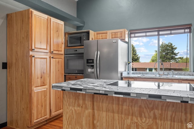 kitchen featuring wood finished floors, stainless steel fridge, black oven, a sink, and tile countertops