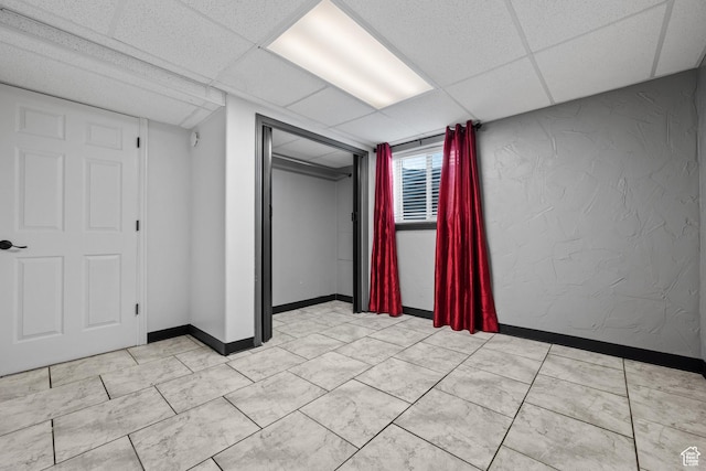 interior space with a paneled ceiling, a textured wall, and baseboards