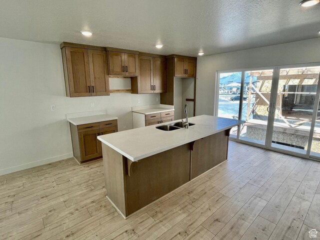 12975 S Spook Gulch Ct Unit 621, Riverton, UT 84096 - kitchen featuring brown cabinetry, baseboards, light wood finished floors, a sink, and an island with sink