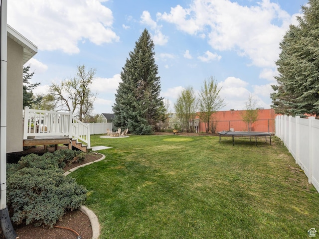 view of yard with a deck, an outdoor fire pit, a trampoline, and a fenced backyard