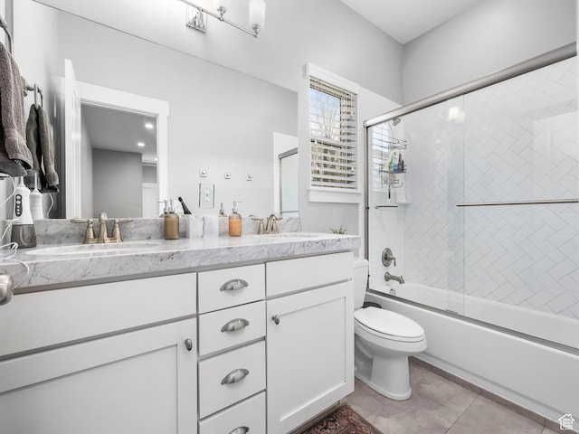 full bath with toilet, double vanity, a sink, and combined bath / shower with glass door