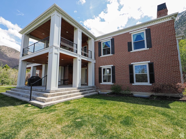 back of property featuring a yard, brick siding, a chimney, and a balcony