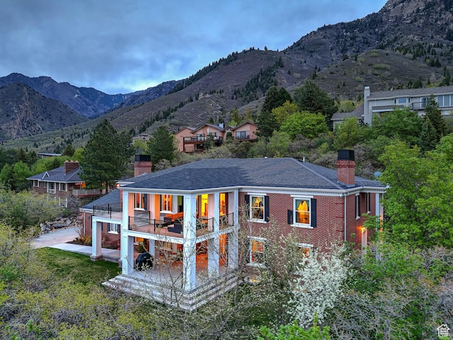 rear view of property featuring roof with shingles, a chimney, a balcony, and a mountain view