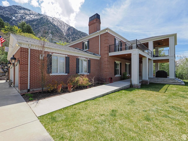 exterior space featuring a chimney, a yard, brick siding, a mountain view, and a balcony