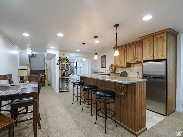 kitchen featuring a kitchen breakfast bar, freestanding refrigerator, light stone countertops, ornamental molding, and recessed lighting