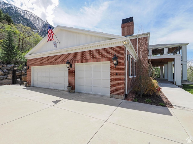 view of side of home featuring a chimney, brick siding, a mountain view, and driveway