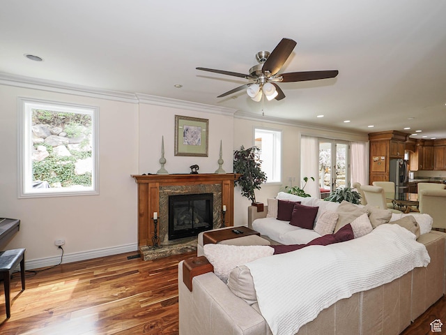 living area featuring crown molding, a premium fireplace, baseboards, wood finished floors, and a ceiling fan