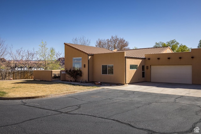 view of front of house featuring a tiled roof, fence, aphalt driveway, an attached garage, and stucco siding