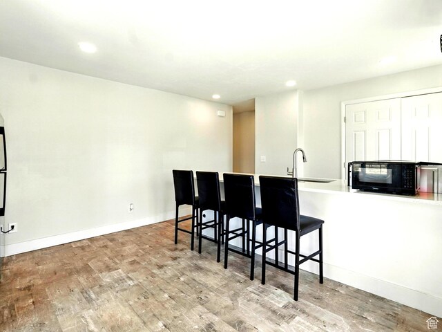 302 34th St, Ogden, UT 84401 - kitchen featuring a sink, black microwave, wood finished floors, recessed lighting, and a kitchen bar