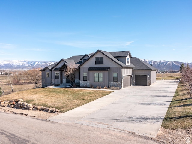 modern farmhouse style home with driveway, stone siding, a front yard, a mountain view, and a garage