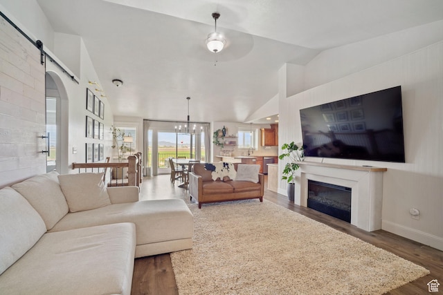9457 N 4800 W, Elwood, UT 84337 - living area with a barn door, lofted ceiling, a glass covered fireplace, wood finished floors, and ceiling fan with notable chandelier