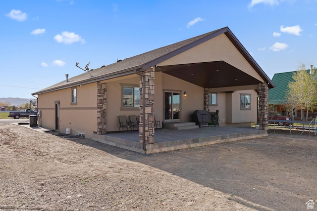 rear view of house featuring stucco siding, roof with shingles, and a patio