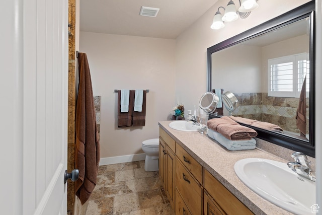 bathroom with visible vents, toilet, stone tile flooring, and a sink