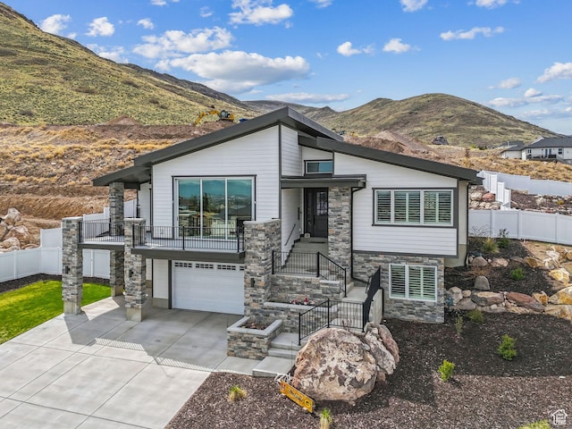view of front facade with driveway, stone siding, a mountain view, an attached garage, and fence