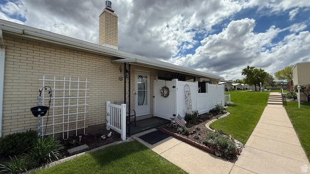 doorway to property with a chimney, brick siding, and a yard