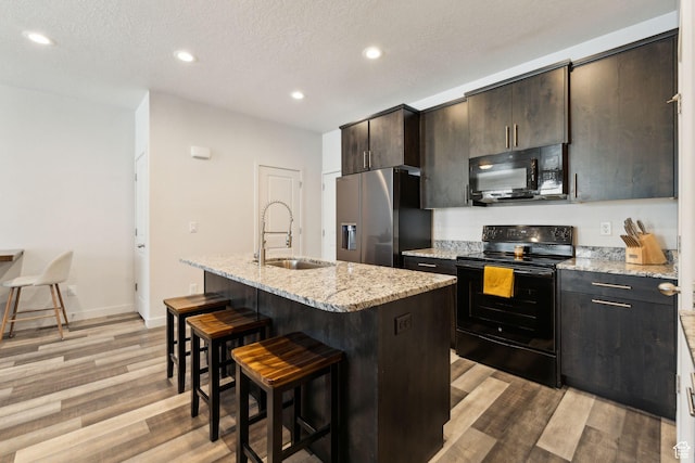 kitchen with a sink, black appliances, a breakfast bar, recessed lighting, and light wood-style flooring