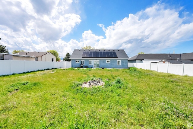rear view of house with a lawn, solar panels, and a fenced backyard