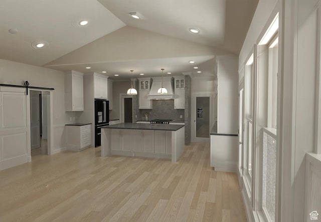 kitchen featuring a barn door, decorative backsplash, premium range hood, dark countertops, and lofted ceiling