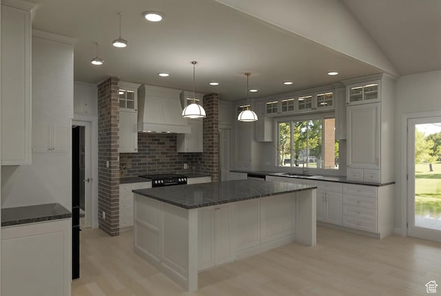 kitchen with decorative backsplash, light wood-style flooring, glass insert cabinets, a sink, and custom exhaust hood