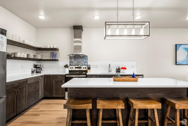 140 W 150 S Unit H29, Garden City, UT 84028 - kitchen featuring stainless steel electric range, a kitchen breakfast bar, open shelves, wall chimney range hood, and dark brown cabinets