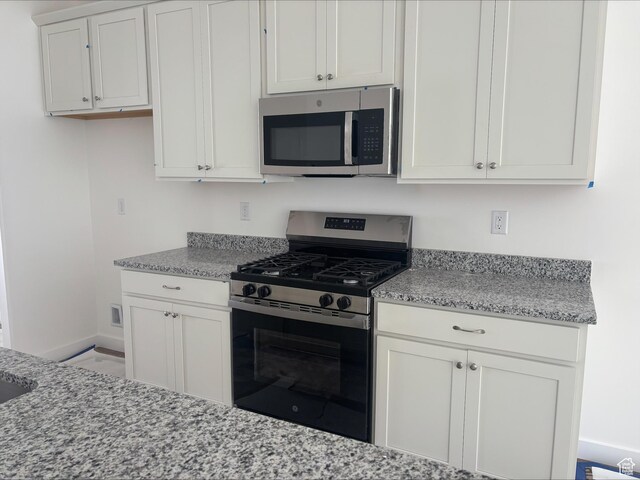 kitchen with baseboards, light stone counters, stainless steel appliances, and white cabinetry