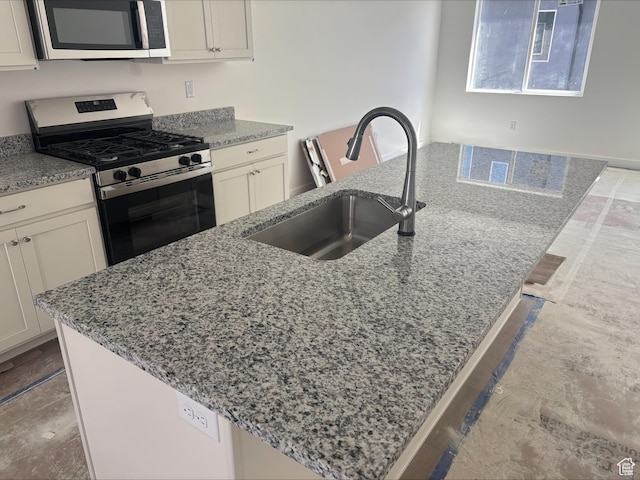 kitchen with light stone countertops, appliances with stainless steel finishes, a sink, a kitchen island with sink, and white cabinetry