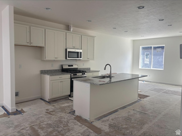 kitchen featuring baseboards, a center island with sink, a sink, stone counters, and stainless steel appliances