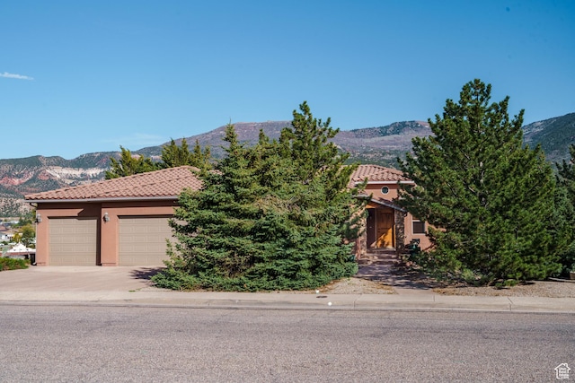 view of front facade featuring stucco siding, a garage, a tile roof, driveway, and a mountain view