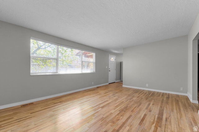 unfurnished living room featuring baseboards, light wood-type flooring, visible vents, and a textured ceiling