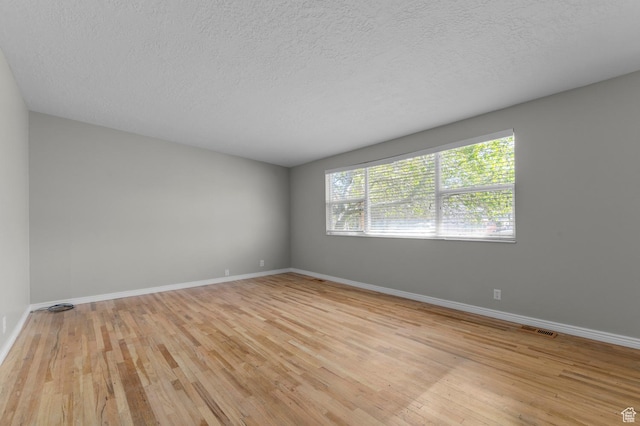 spare room with a textured ceiling, visible vents, baseboards, and light wood-type flooring