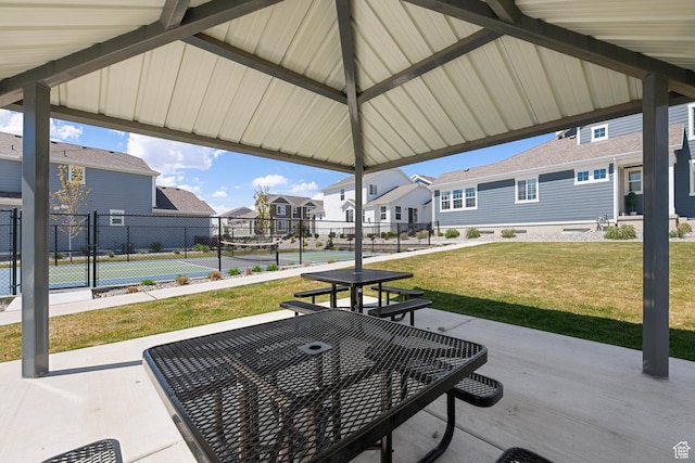 view of patio / terrace with a tennis court, fence, and a residential view