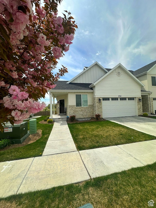 view of front of property with a garage, board and batten siding, a front lawn, and stone siding