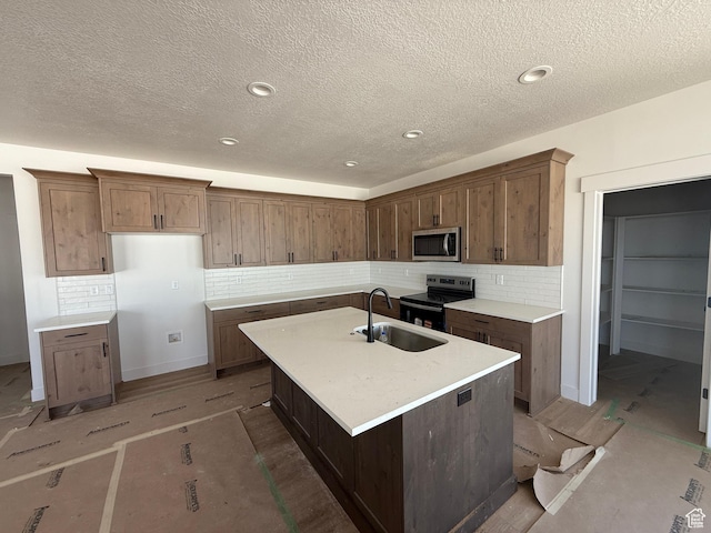 1107 S 4475 W, West Point, UT 84015 - kitchen featuring stainless steel microwave, range with electric stovetop, tasteful backsplash, a center island with sink, and a textured ceiling
