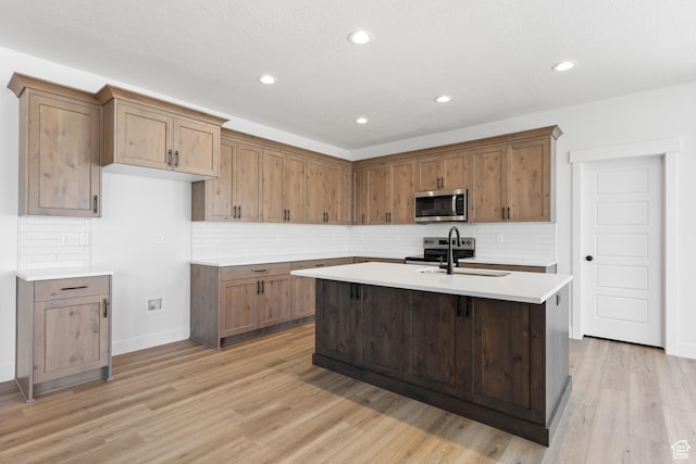 1107 S 4475 W, West Point, UT 84015 - kitchen featuring appliances with stainless steel finishes, light countertops, light wood-type flooring, a center island with sink, and tasteful backsplash