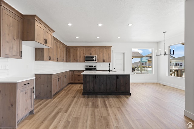 1107 S 4475 W, West Point, UT 84015 - kitchen with stainless steel microwave, decorative backsplash, light wood-type flooring, light countertops, and a kitchen island with sink